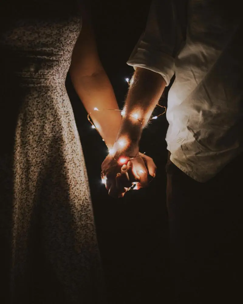 A couple holding hands with lights in the middle of them.