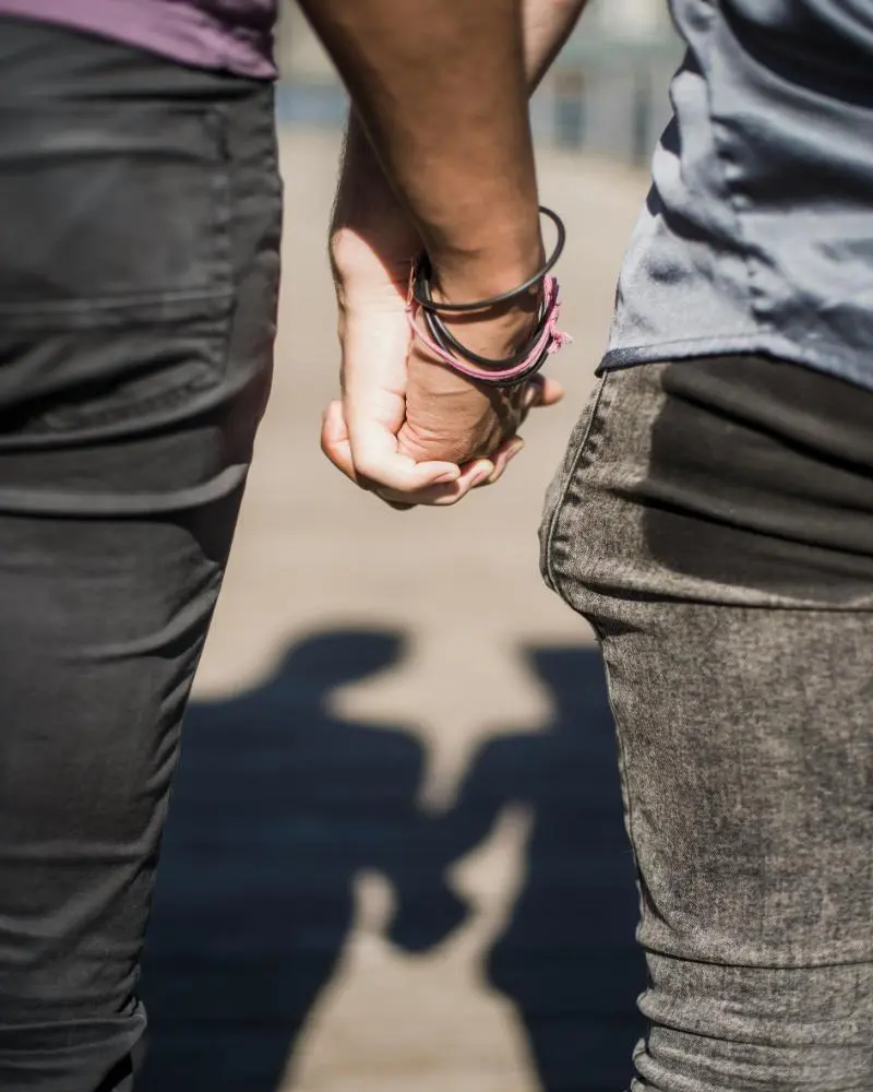 Two people holding hands while standing on a sidewalk.