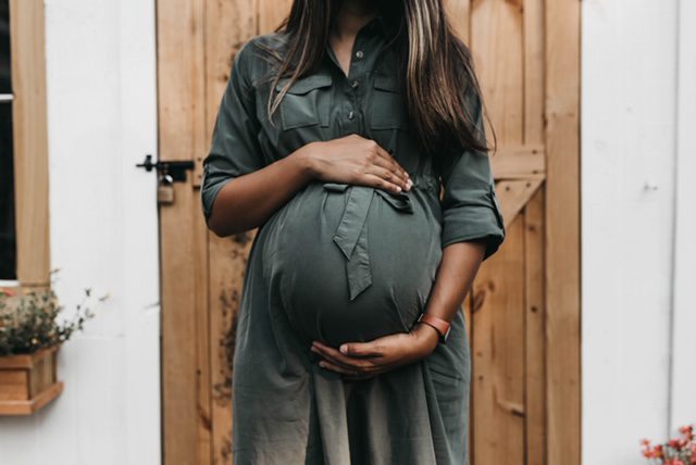 A woman holding her pregnant belly in front of a wooden door.